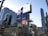 A bustling urban scene with tall buildings and numerous advertisements including prominent brands like Bell and McDonald's. The architecture features a mix of glass and steel structures, with large digital billboards displaying various products and services. There are traffic lights and street signs visible, contributing to the city's busy ambience.