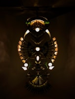 An elaborate art installation features symmetrical arrangements of lights and metallic elements. The design creates an abstract, eye-catching pattern with a central circular motif and radial lines extending outward. The dark background enhances the illuminated components, giving a sense of depth and mystery.