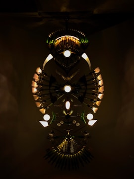 An elaborate art installation features symmetrical arrangements of lights and metallic elements. The design creates an abstract, eye-catching pattern with a central circular motif and radial lines extending outward. The dark background enhances the illuminated components, giving a sense of depth and mystery.