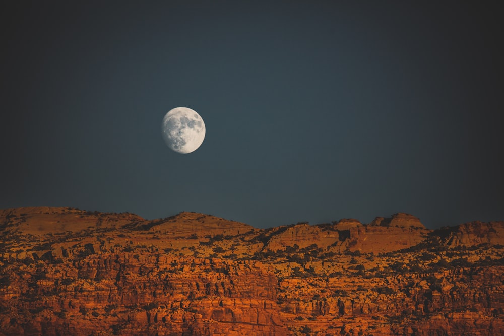 a full moon rising over a rocky mountain range