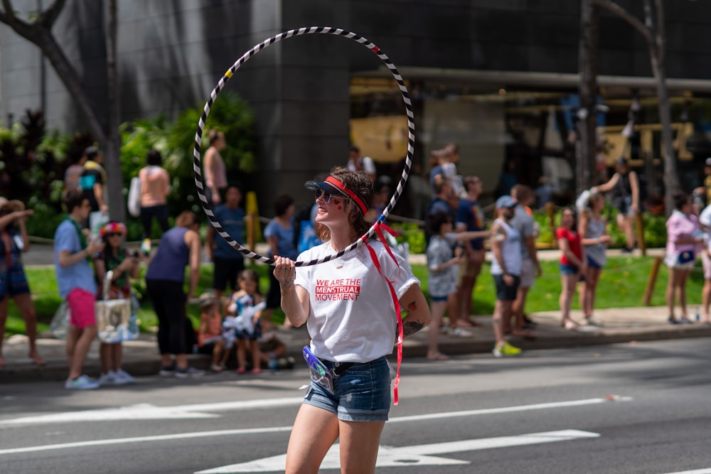 Frau trägt weißes und rotes T-Shirt mit Rundhalsausschnitt und Sonnenbrille, die beim Lochen des Hula-Hoop-Reifens steht