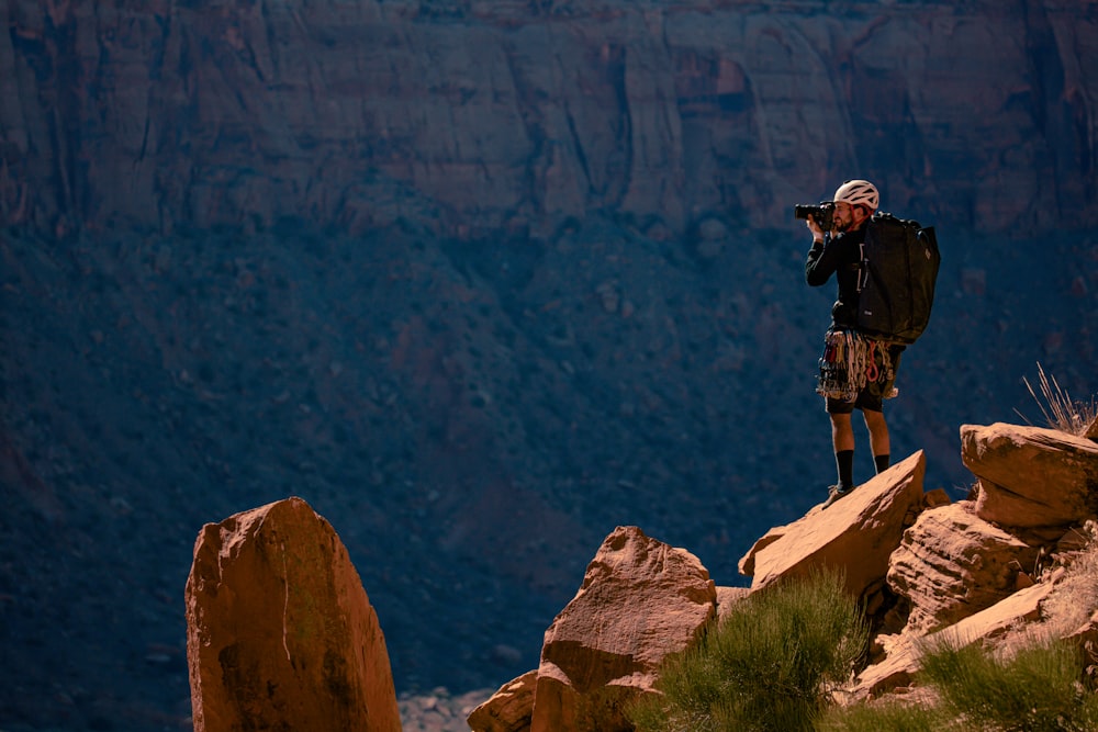 man standing and taking photo of rocky hill