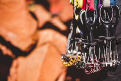 A collection of climbing cams hangs with multiple colorful slings. The background features out-of-focus natural rock formations.