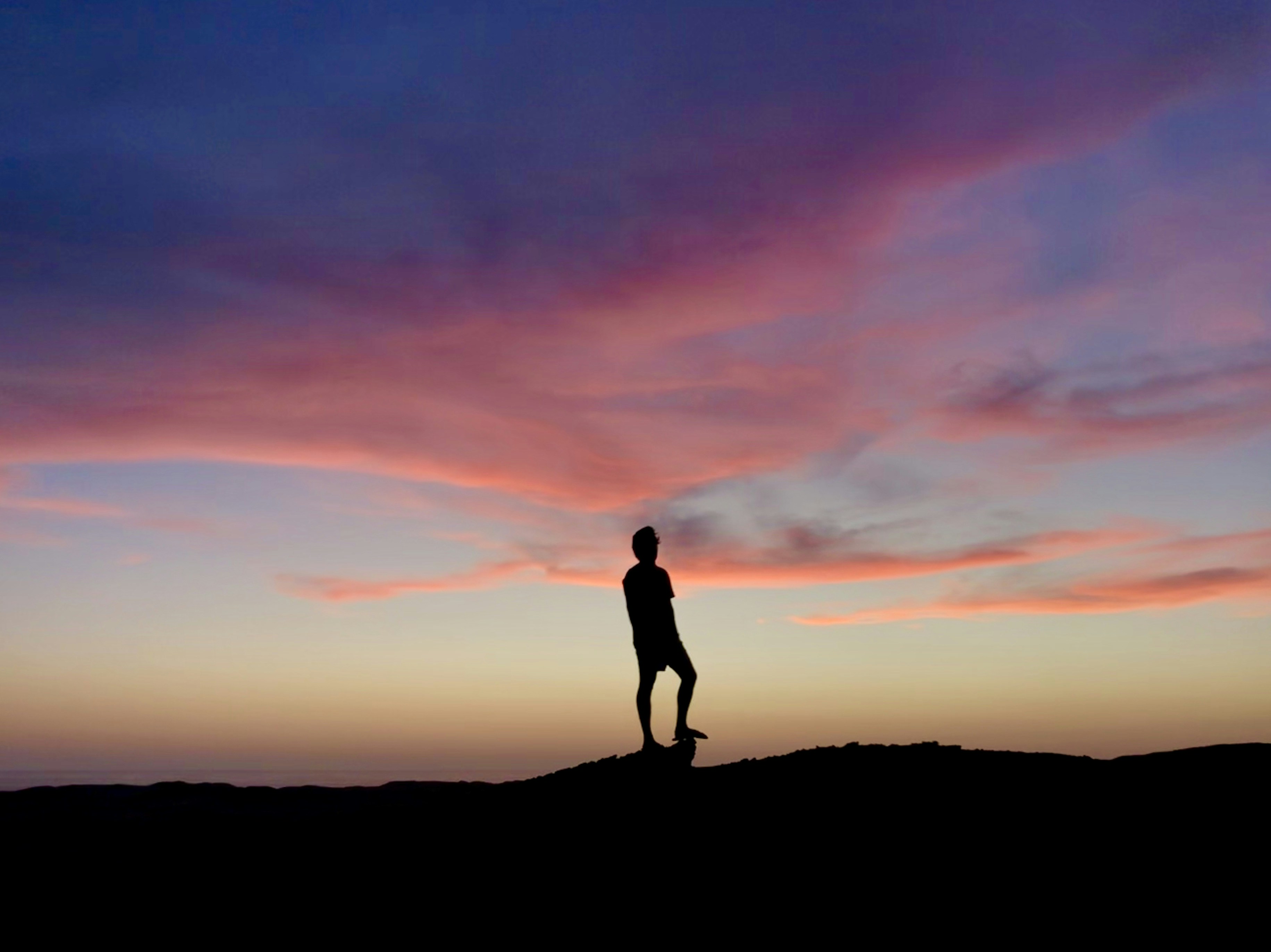Single person standing on a hilltop silhouette against a dramatic sunset sky