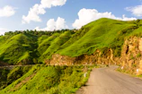 A winding road through lush green hills under a bright blue sky in Southern Transylvania