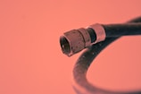 A close-up view of a coaxial cable connector with a metal tip and threaded base. The background is a solid color, adding emphasis to the cable's features and structure.