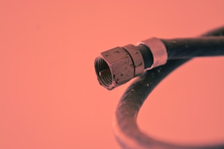 A close-up view of a coaxial cable connector with a metal tip and threaded base. The background is a solid color, adding emphasis to the cable's features and structure.