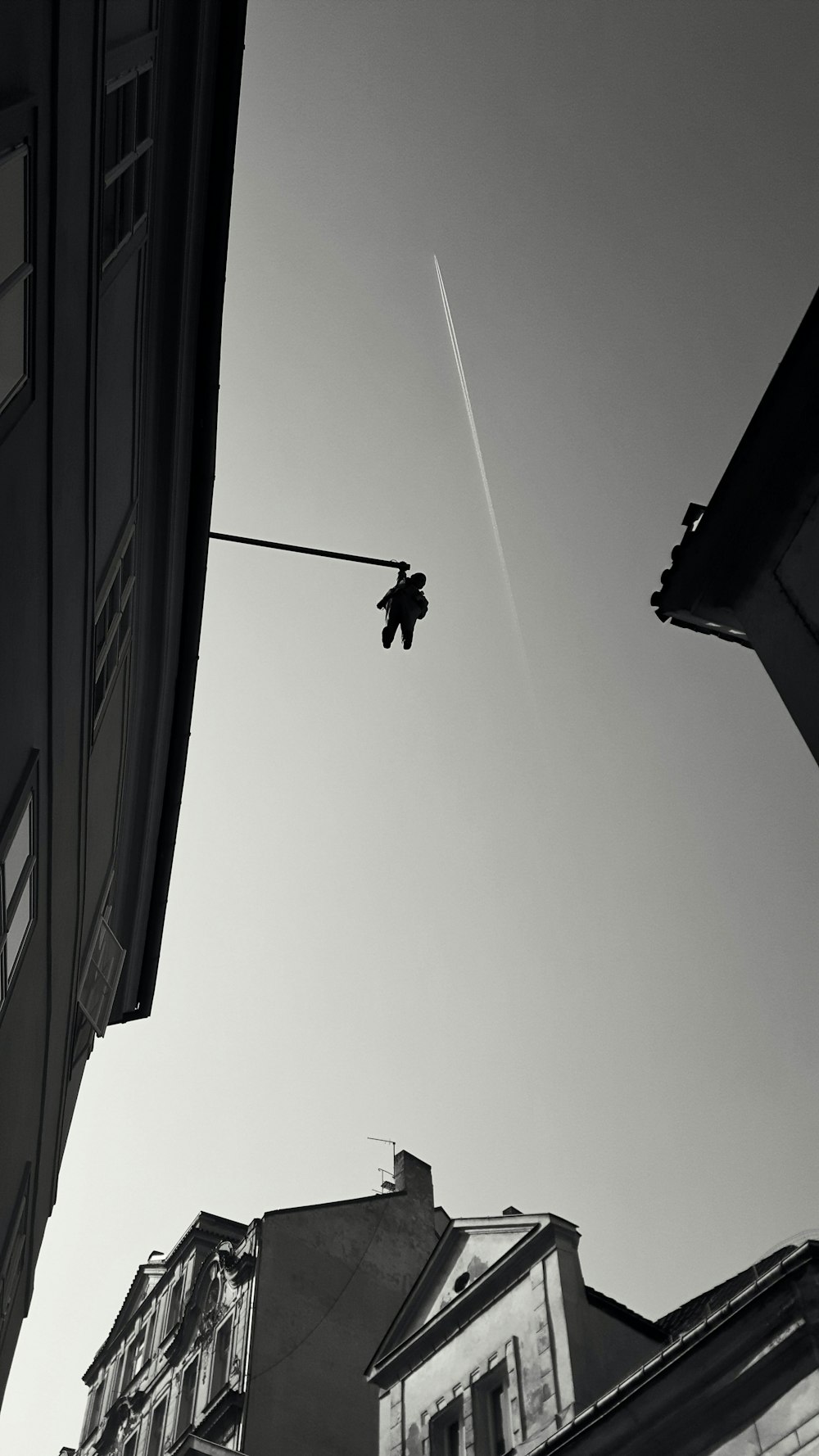 grayscale photography of person hanging on edge of rooftop