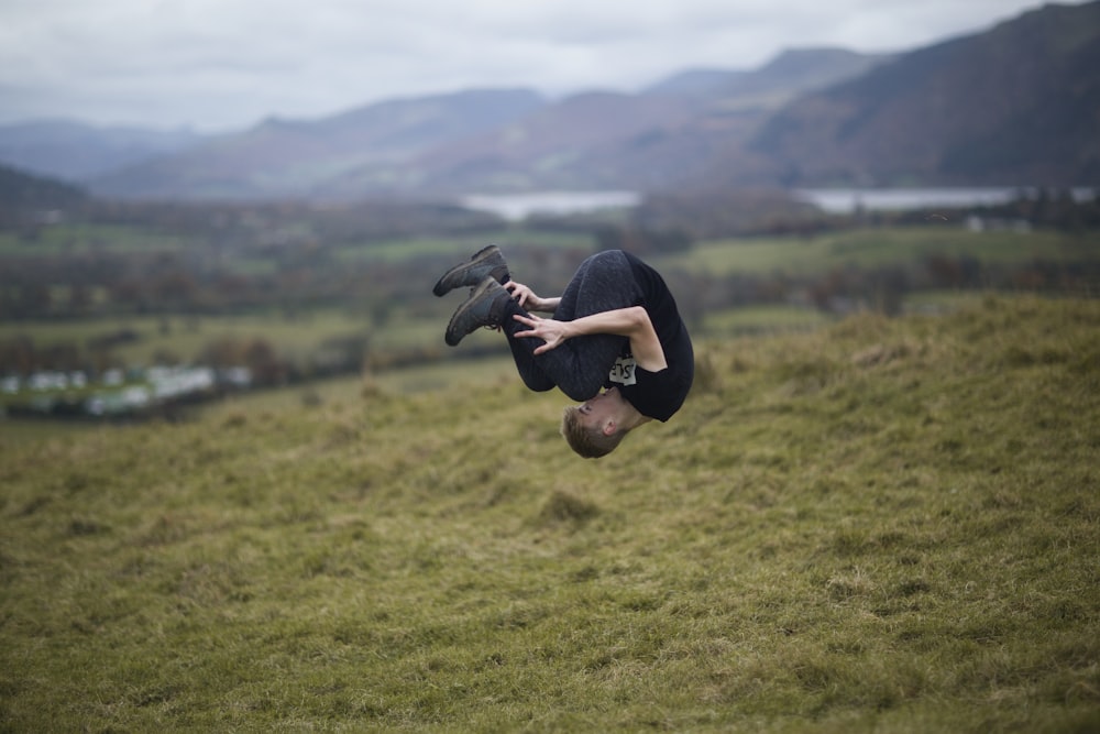 man wearing black crew-neck t-shirt tumbling on green field