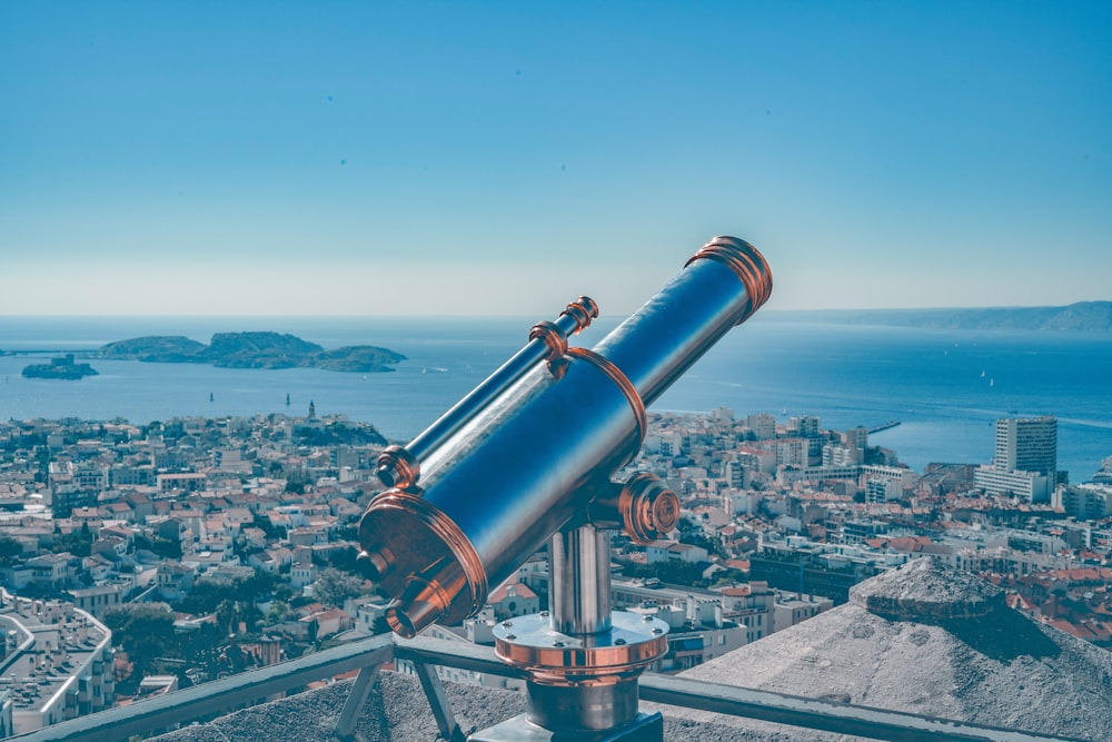 blue and brown coin-operated telescope viewing city with high-rise buildings, blue sea, and mountain under blue and white sky