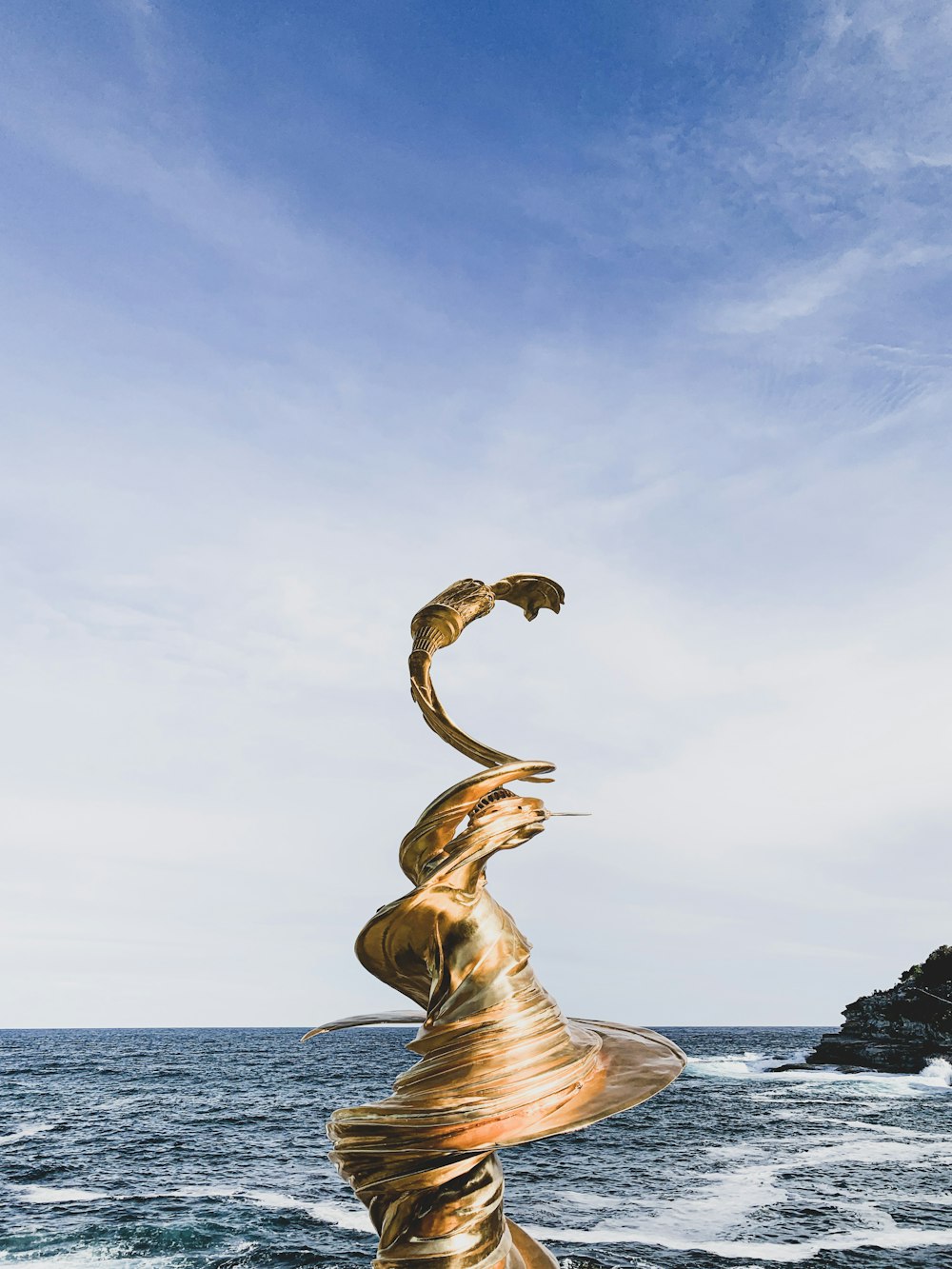 하얗고 푸른 하늘 아래 해변 근처의 소용돌이 치는 황금 동상