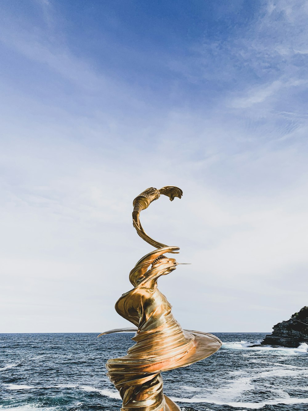 Statue d’or tourbillon près du bord de mer sous le ciel blanc et bleu