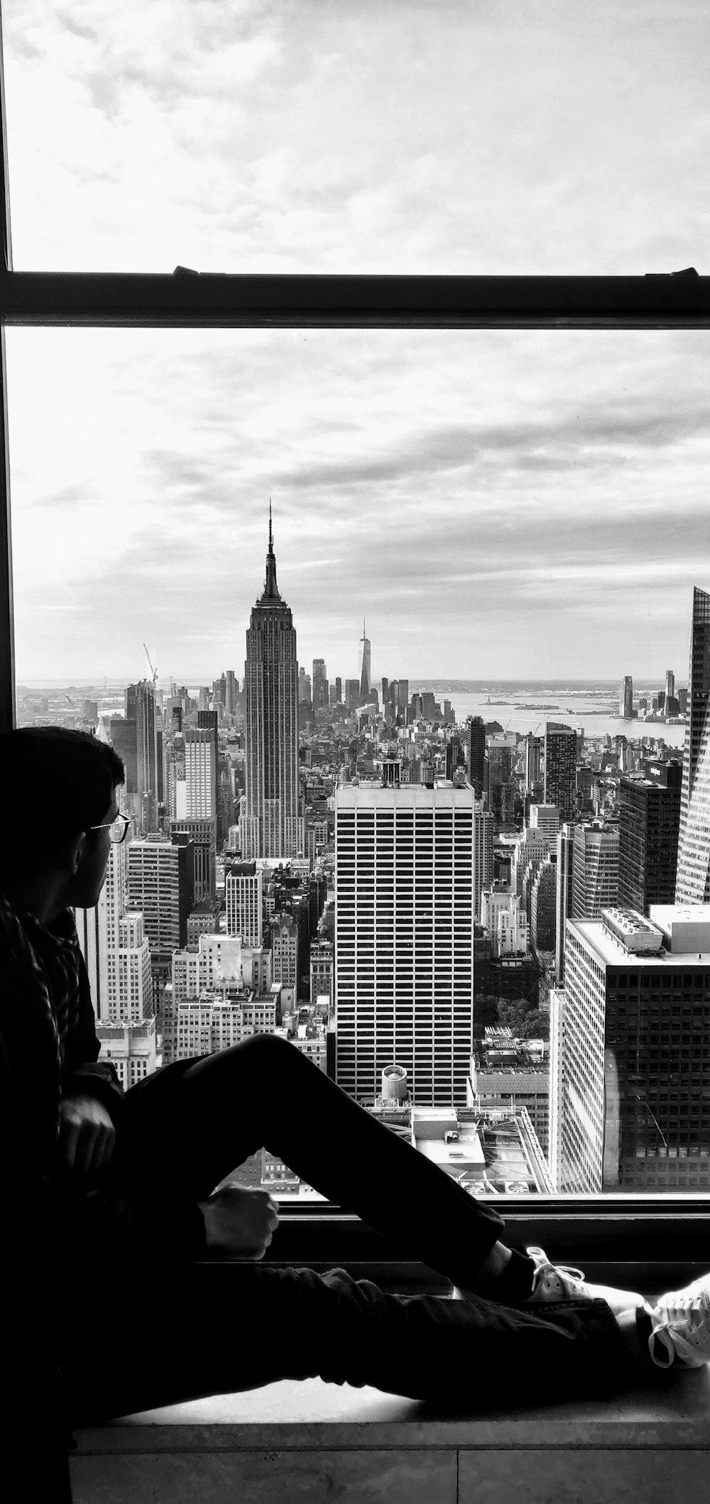 grayscale photography of man sitting near closed window viewing New York City