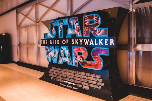 A large cardboard promotional display for the movie 'Star Wars: The Rise of Skywalker' featuring characters in vibrant colors. It is positioned against a metallic wall with industrial aesthetics.