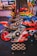 A row of arcade motorcycle racing games is lined up, featuring brightly colored machines with detailed graphics and logos. A person in the background stands near decorated countertops and a wall-mounted screen. The environment has a lively and playful ambiance, with vibrant colors and patterns.