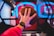 A hand wears a digital watch and holds a basketball, aiming towards a basketball hoop with vibrant neon lights in the background, creating a dynamic and energetic atmosphere.