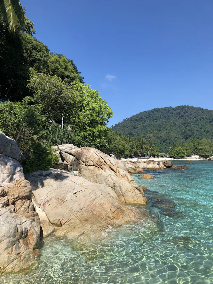 Strand mit großen Felsblöcken und bewaldeten Hügeln