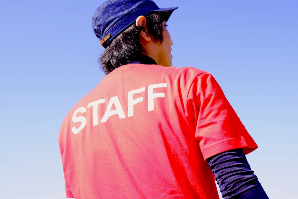 male staff wearing red t-shirt and blue hat standing