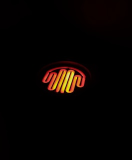 Glowing orange and yellow heating element, shaped in a wavy pattern, illuminated against a dark background.