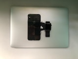 A smartphone and a smartwatch are placed on top of a closed laptop, all of which are identifiable as Apple products.