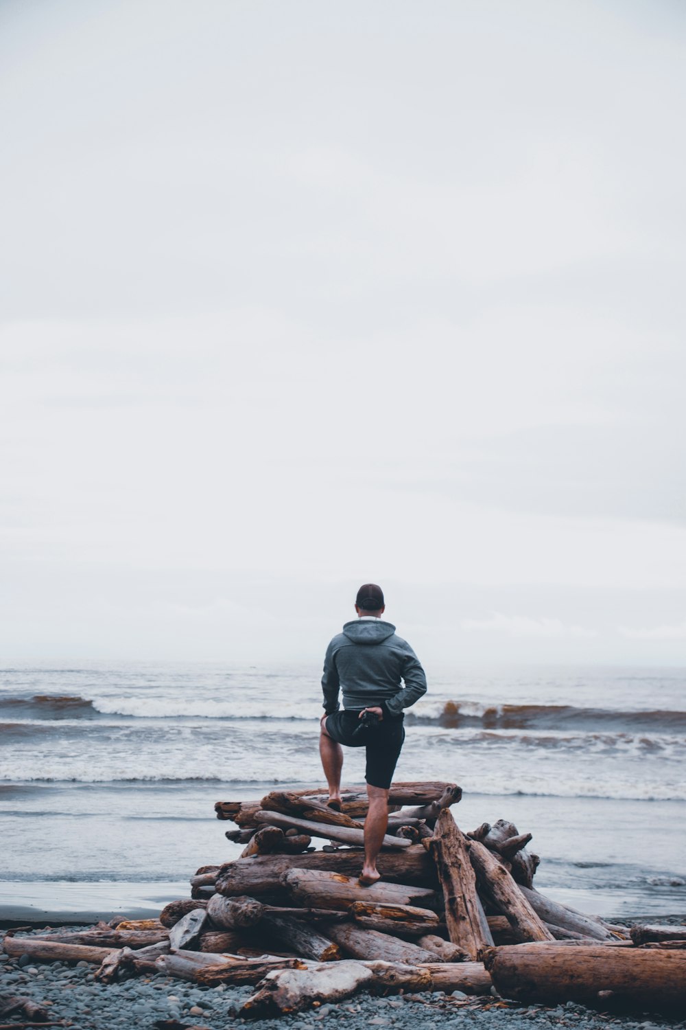 person standing on logs near seashore