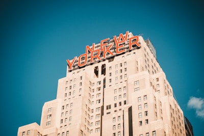 A tall Art Deco style skyscraper with the words 'NEW YORKER' prominently displayed in large red letters at the top against a clear blue sky.