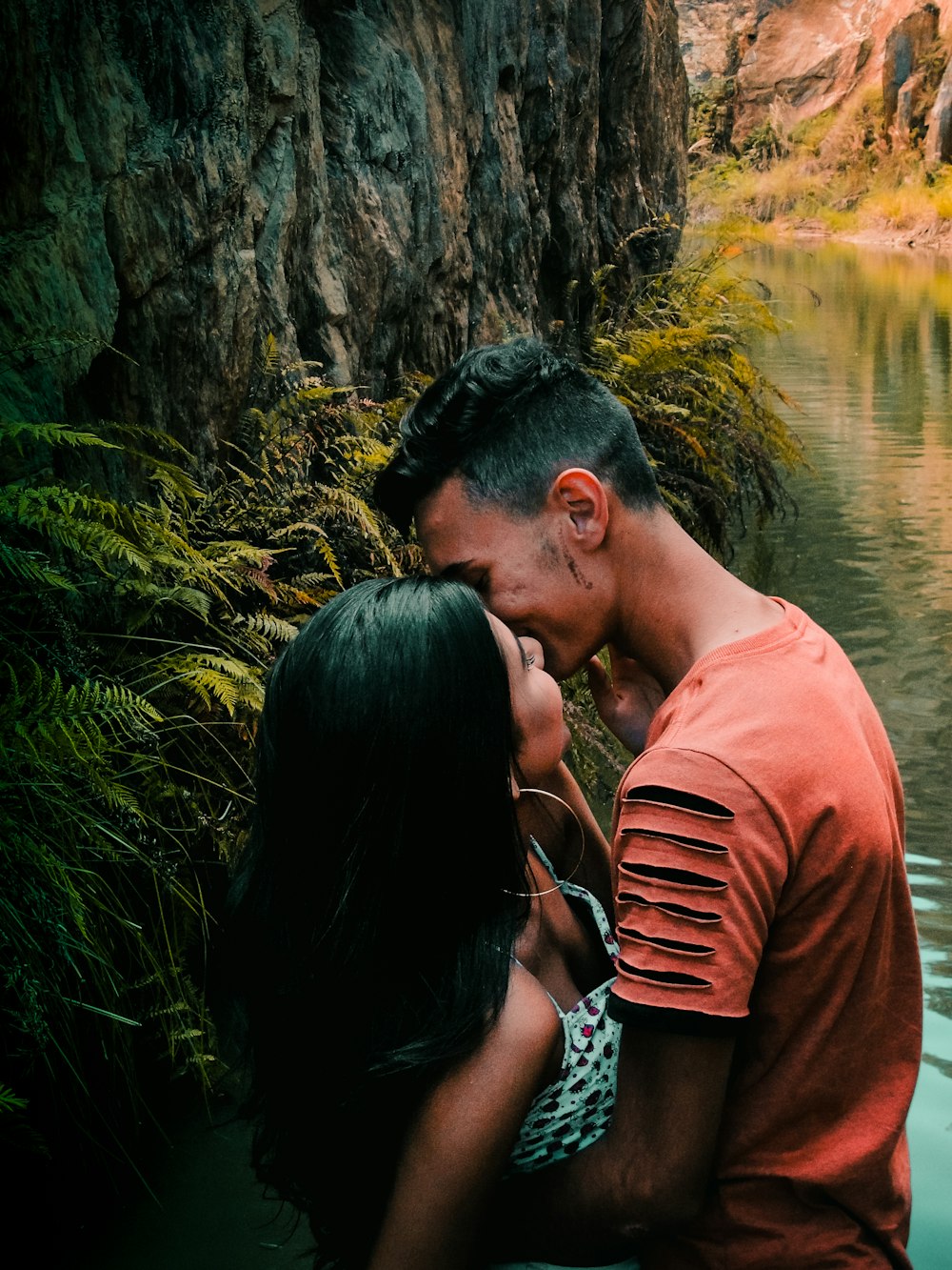 homem e mulher em pé e de frente um para o outro enquanto se beijam nos lábios perto do corpo de água