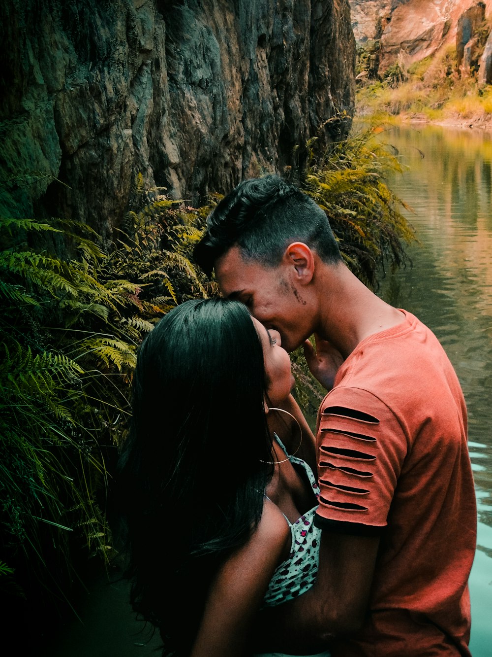 hombre y mujer de pie y uno frente al otro mientras se besan en los labios cerca del cuerpo de agua