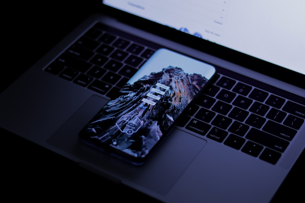 black smartphone on top of silver laptop