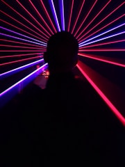 A silhouette of a person is in the foreground, facing an array of vibrant red and blue laser beams radiating outward, creating a dynamic and futuristic visual effect.