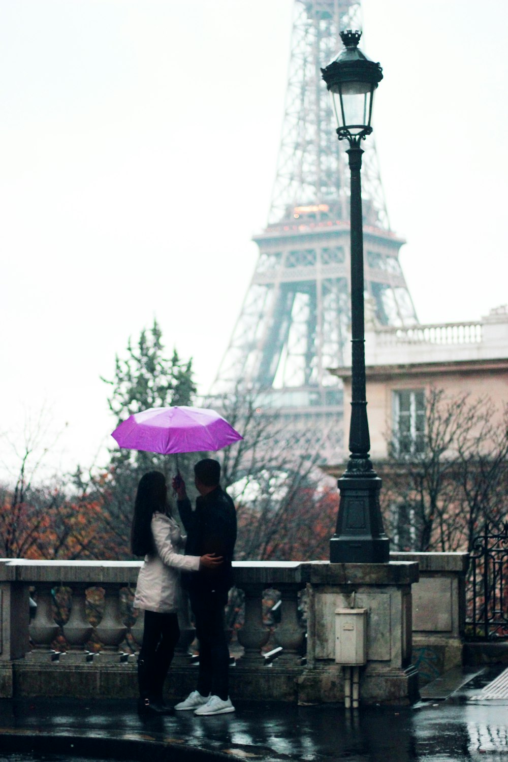 man and woman holding umbrella standing beside railing