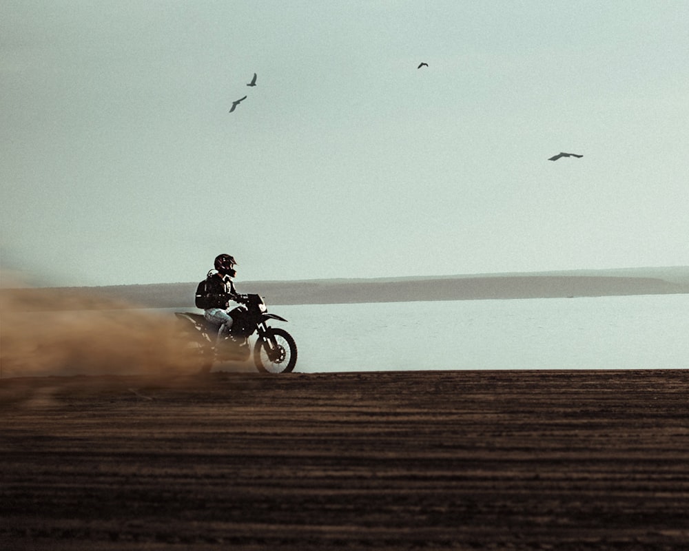 man riding on dirt bike near body of water