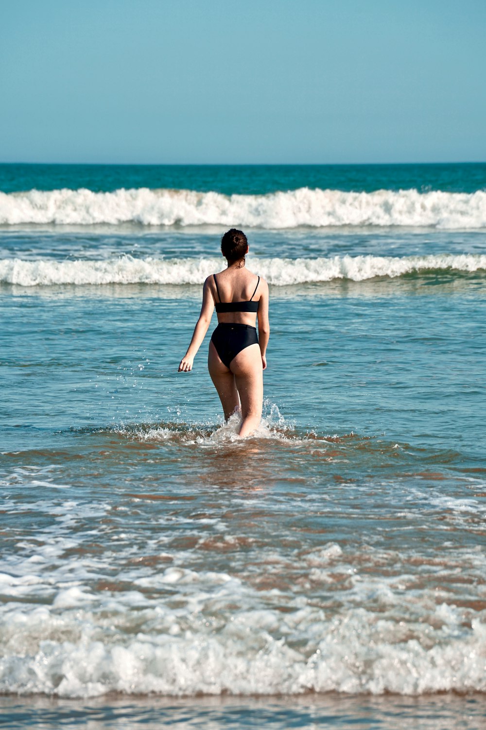 woman wearing black bikini set walking going on blue sea