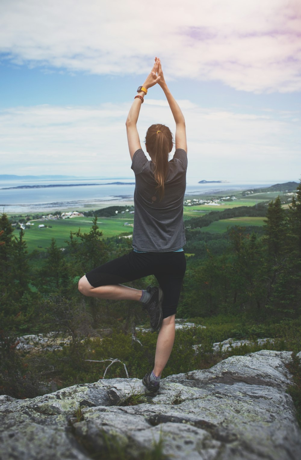 woman standing on one leg on rock facing the field