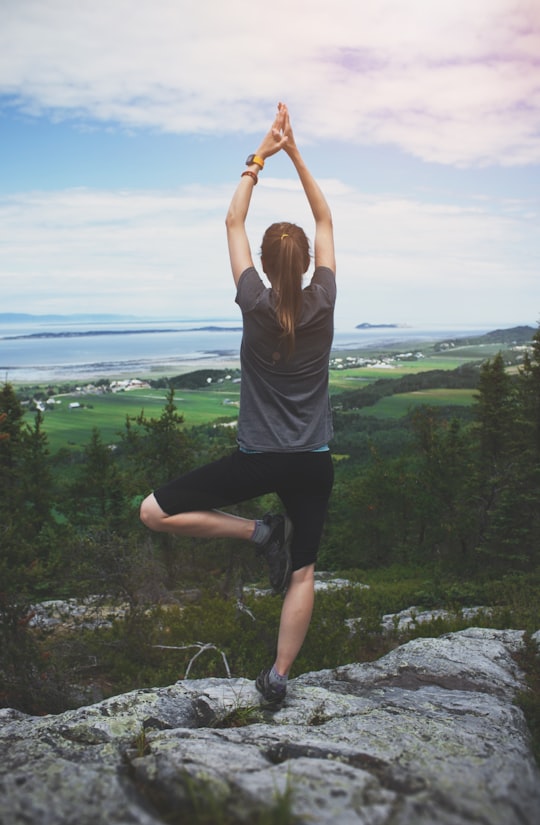 woman standing on one leg on rock facing the field in Saint-André Canada