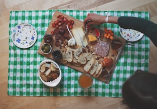 woman about to slice the cheese on wooden board surrounded with bread and sausages