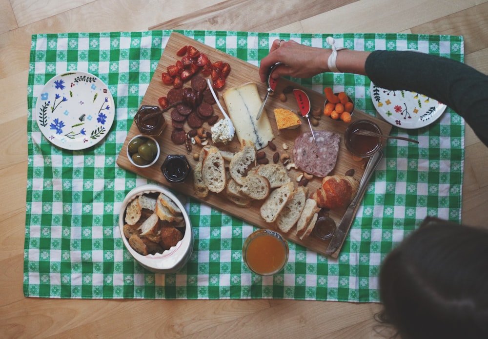 femme sur le point de trancher le fromage sur une planche de bois entourée de pain et de saucisses