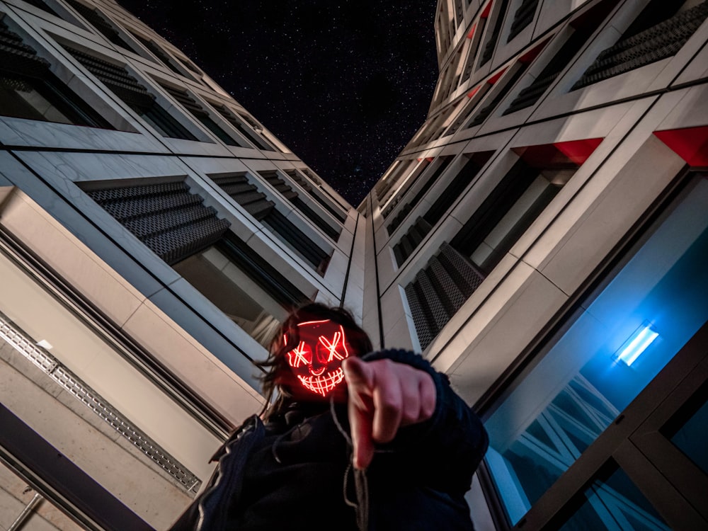 검은색 재킷을 입은 사람이 고층 건물 근처에서 손가락으로 가리키며 서 있다.