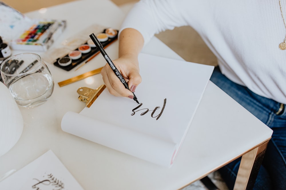 woman holding pen writes in paper on table