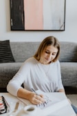 woman in white scoop-neck long-sleeved shirt sitting on floor near sofa and painting