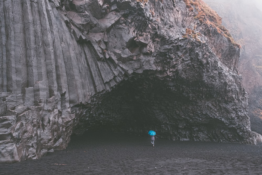person walks with umbrella into cave