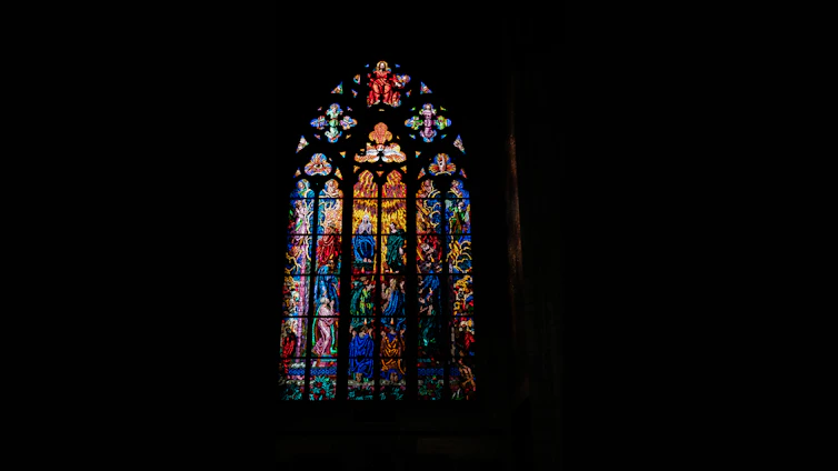 A craftsman carefully restoring a colorful stained glass window in a bright workshop.