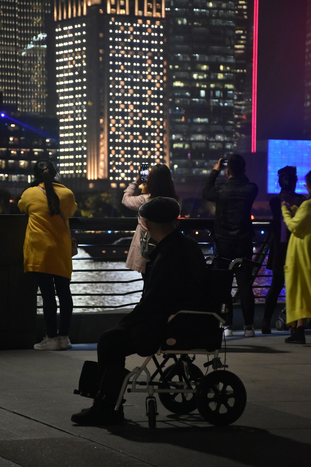 person riding wheelchair near people taking pictures of the city during night