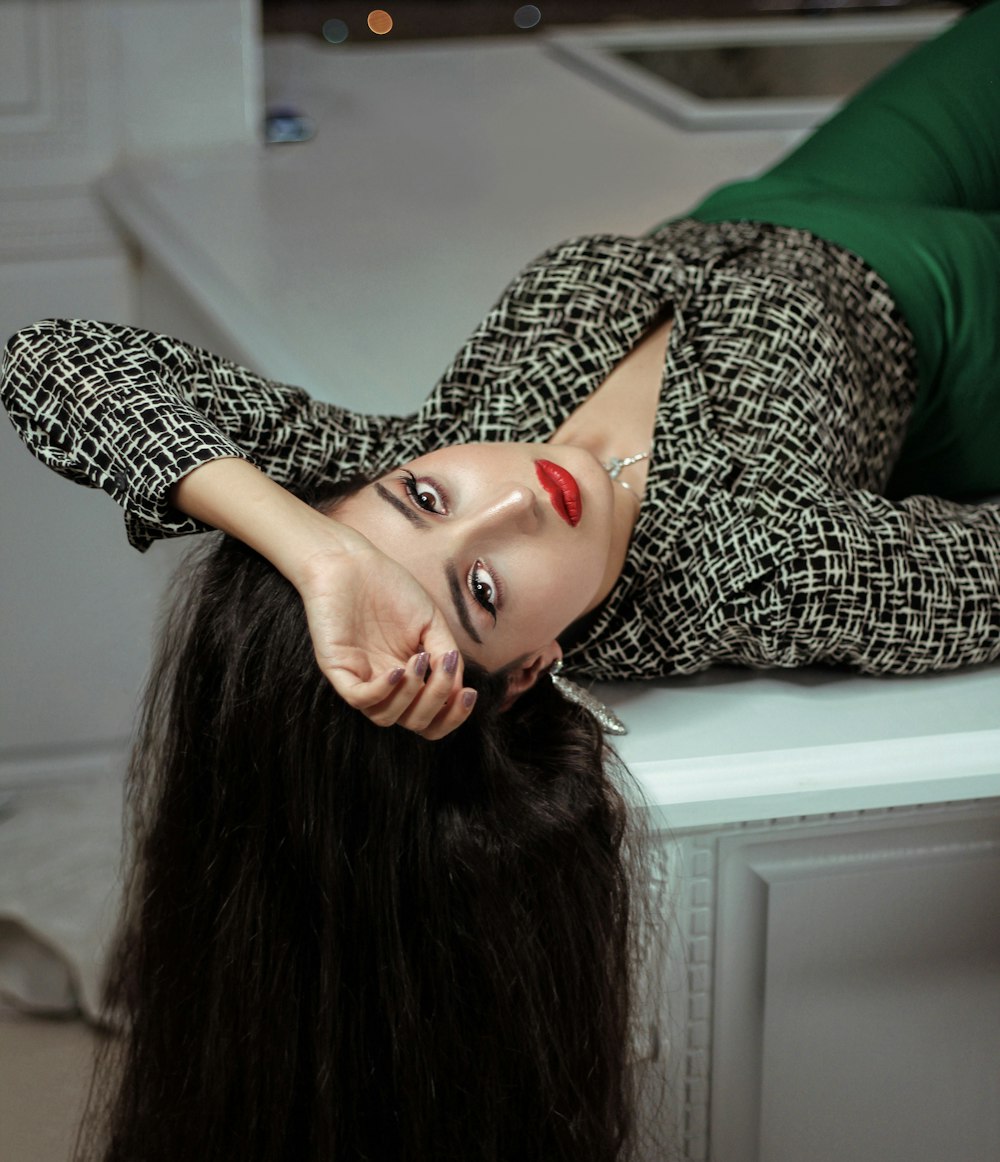 woman wearing gray and white collared button-up long-sleeved blouse lying on white kitchen island