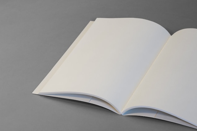 An open blank book with off-white pages lies on a flat gray surface. The book is positioned slightly diagonally, creating a simple and minimalistic composition.