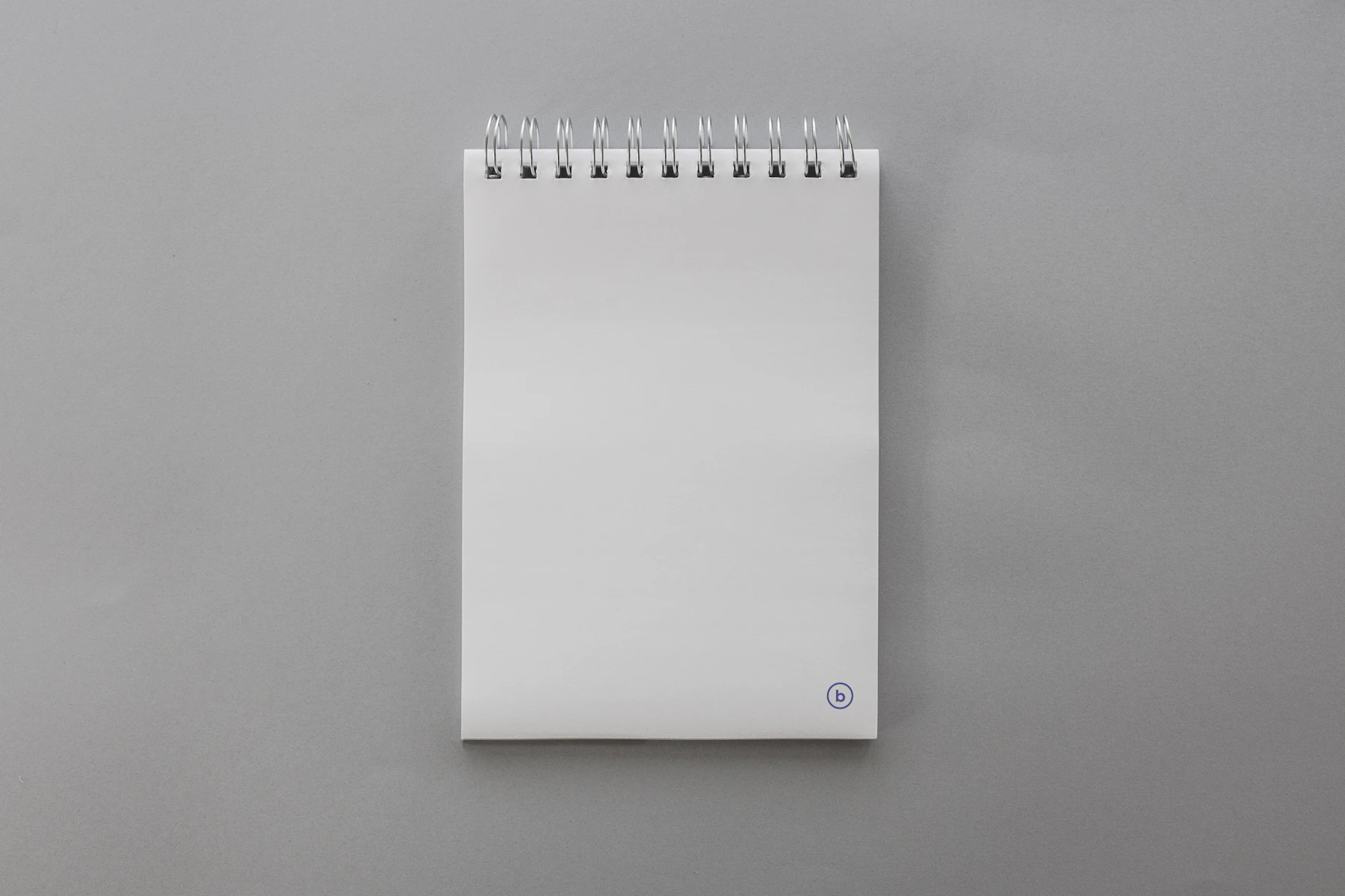 A blank notepad bound with a wire spiral along its top edge, lying on a gray surface