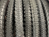 A row of neatly arranged, textured bicycle tires with prominent tread patterns. The tires are displayed vertically, showcasing the intricate details of the rubber surface.