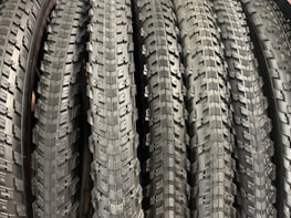 A row of neatly arranged, textured bicycle tires with prominent tread patterns. The tires are displayed vertically, showcasing the intricate details of the rubber surface.