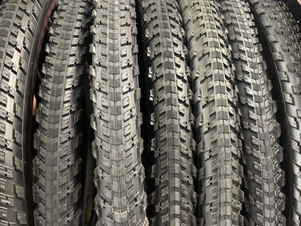 A row of neatly arranged, textured bicycle tires with prominent tread patterns. The tires are displayed vertically, showcasing the intricate details of the rubber surface.