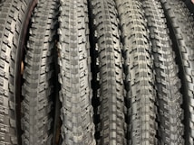 A row of neatly arranged, textured bicycle tires with prominent tread patterns. The tires are displayed vertically, showcasing the intricate details of the rubber surface.